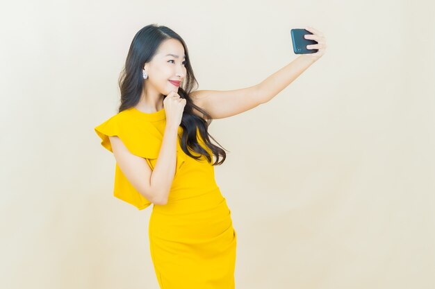 Portrait belle jeune femme asiatique sourit avec un téléphone portable intelligent sur un mur beige