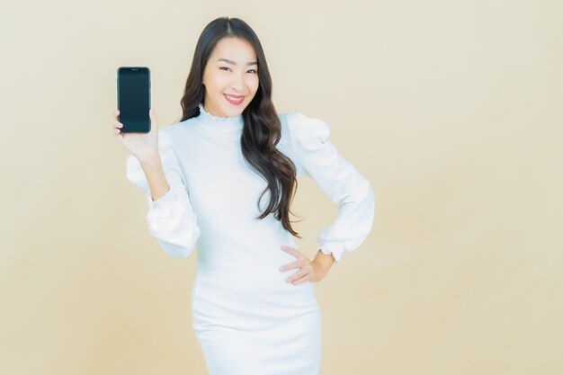 Portrait de la belle jeune femme asiatique sourit avec un téléphone portable intelligent sur un mur de couleur