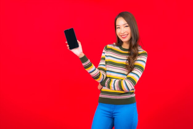 Portrait belle jeune femme asiatique avec téléphone mobile intelligent sur mur rouge