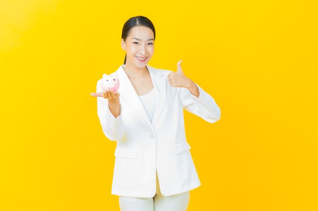 Portrait belle jeune femme asiatique avec tirelire sur mur de couleur