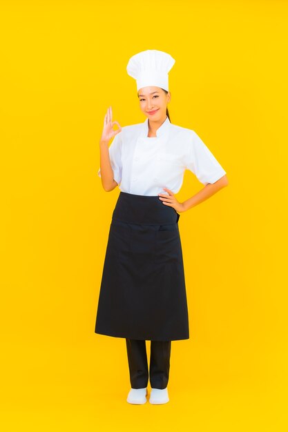 Portrait belle jeune femme asiatique en uniforme de chef ou de cuisinier avec chapeau sur fond isolé jaune