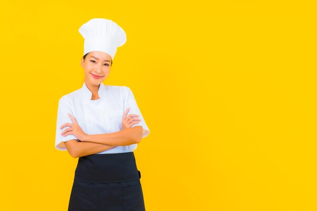 Portrait belle jeune femme asiatique en uniforme de chef ou cuisinier avec chapeau sur fond isolé jaune