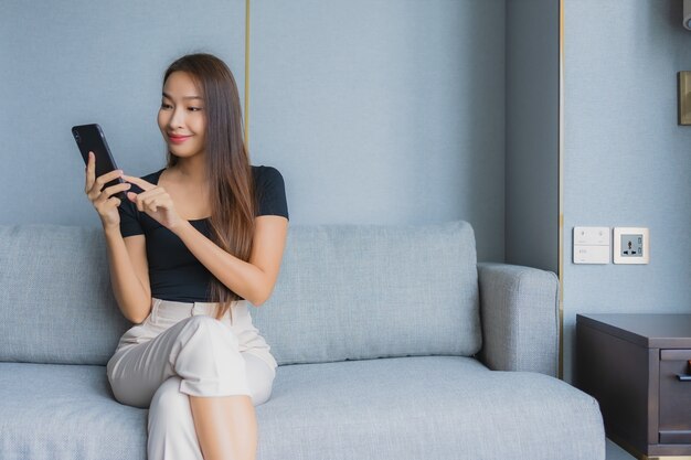 Portrait belle jeune femme asiatique utilise un téléphone mobile intelligent sur un canapé dans le salon