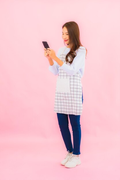 Portrait belle jeune femme asiatique utilise un téléphone mobile intelligent sur un mur isolé rose