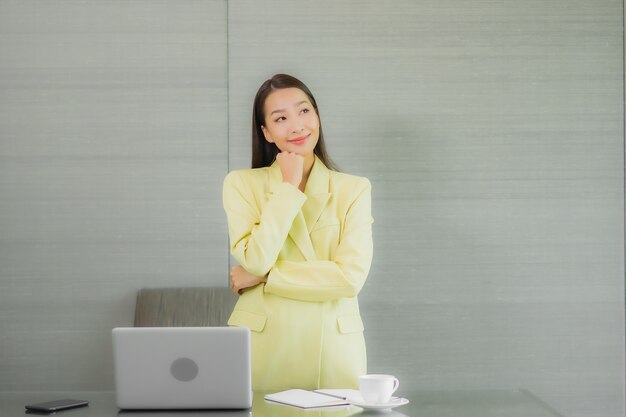 Portrait belle jeune femme asiatique utiliser un ordinateur portable avec un téléphone mobile intelligent sur la table de travail à l'intérieur de la salle