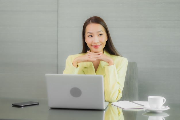 Portrait belle jeune femme asiatique utiliser un ordinateur portable avec un téléphone mobile intelligent sur la table de travail à l'intérieur de la salle