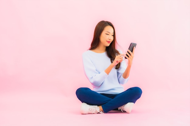 Portrait belle jeune femme asiatique utiliser un téléphone mobile intelligent sur un mur isolé de couleur rose