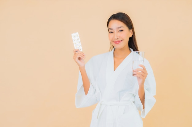 Portrait belle jeune femme asiatique avec verre d'eau et pilule de drogue sur beige