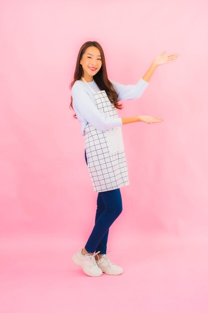 Portrait belle jeune femme asiatique en vêtements de cuisine avec tablier sur mur isolé rose