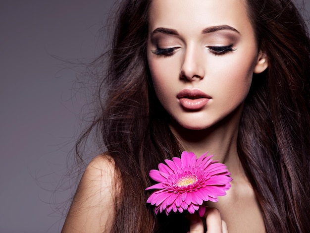 Portrait de la belle jeune femme aux longs cheveux bruns avec fleur rose posant sur un mur sombre