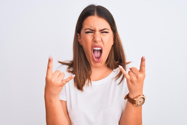 Portrait de belle et jeune femme brune debout sur fond blanc isolé criant avec une expression folle faisant le symbole du rock avec les mains en l'air Music star Heavy concept