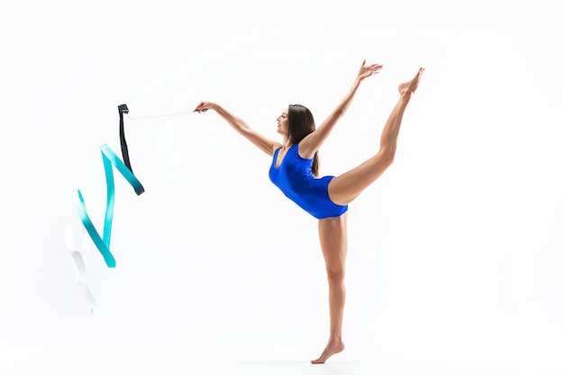 Le portrait de la belle jeune femme brune gymnaste exercice de callisthénie avec ruban bleu sur studio blanc