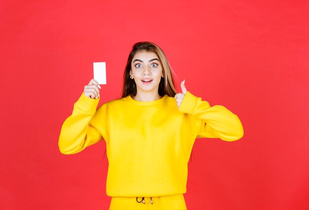 Portrait d'une belle jeune femme avec une carte de visite vierge donnant les pouces vers le haut