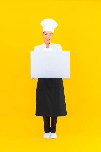 Photo gratuite portrait belle jeune femme chef asiatique avec panneau d'affichage vide blanc sur fond isolé jaune