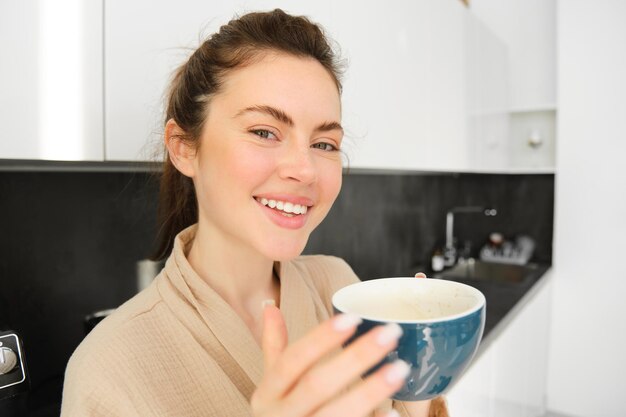 Portrait d'une belle jeune femme commençant sa journée avec une tasse de café debout dans la cuisine et