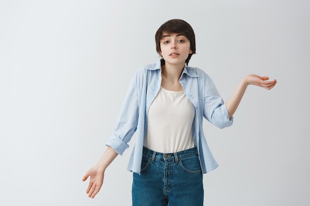 Portrait de la belle jeune femme à la coupe courte gesticulant avec les mains montrant qu'elle ne comprend rien. Le langage du corps.