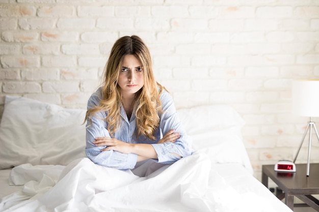 Portrait d'une belle jeune femme hispanique en pyjama qui a l'air très contrariée alors qu'elle est assise dans son lit