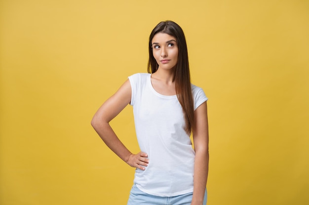 Portrait de la belle jeune femme pensant sur le fond jaune