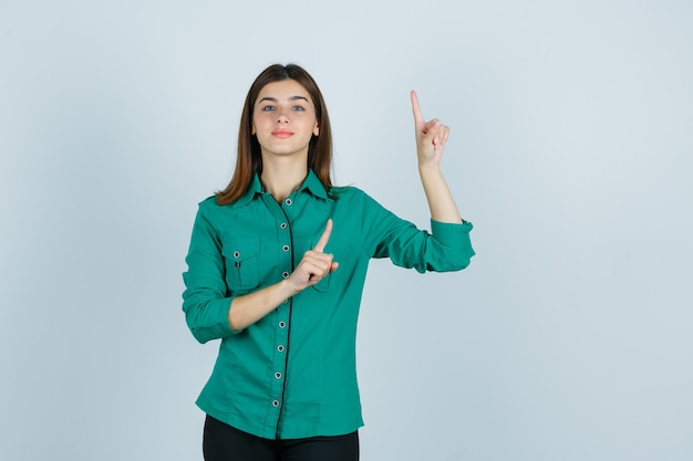 Portrait de la belle jeune femme pointant vers le haut en chemise verte et à la vue de face confiante