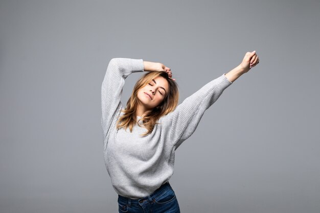 Portrait d'une belle jeune femme porter en pull en gardant les bras levés contre le mur gris