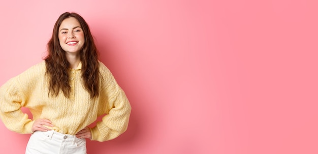 Portrait d'une belle jeune femme posant et riant insouciante tenant les mains sur la taille, ressentant de la joie