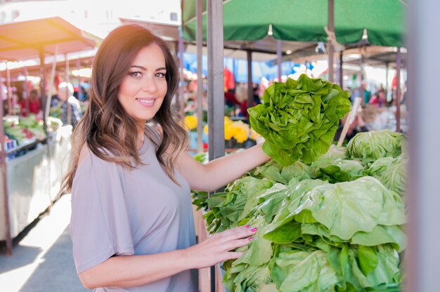 Portrait d&#39;une belle jeune femme qui choisit des légumes à feuilles vertes dans un marché vert. Concept de shopping alimentaire sain. Jeune femme achetant des légumes au marché vert.