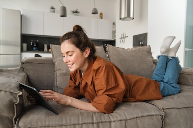 Photo gratuite portrait d'une belle jeune femme se reposant à la maison sur le canapé allongé sur le canapé avec lecture de tablette numérique