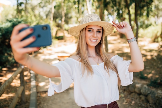 Portrait d'une belle jeune femme selfie dans le parc avec un smartphone