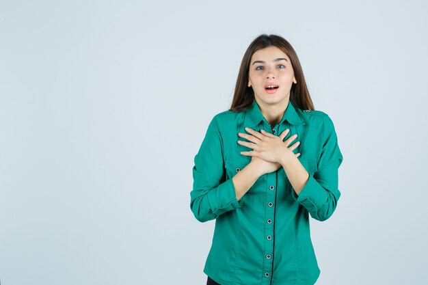 Portrait De La Belle Jeune Femme Tenant Les Mains Sur La Poitrine En Chemise Verte Et à La Vue De Face émerveillée