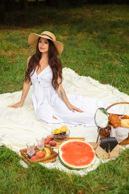 Portrait d'une belle jeune fille aux dents blanches même, un beau sourire dans un chapeau de paille et une longue robe blanche font un pique-nique dans le jardin