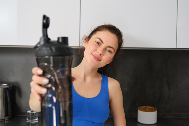 Photo gratuite portrait d'une belle jeune fille de fitness vous offrant une bouteille d'eau à boire après l'entraînement debout