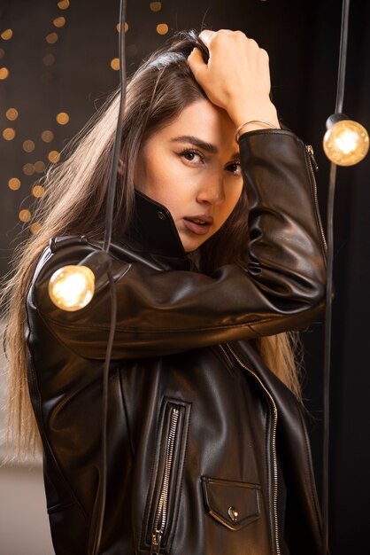 Portrait d'une belle jeune mannequin en blouson de cuir noir posant près des lampes.