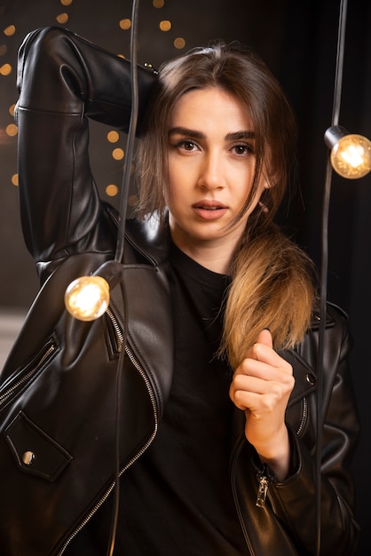 Portrait d'une belle jeune mannequin en blouson de cuir noir posant près des lampes.