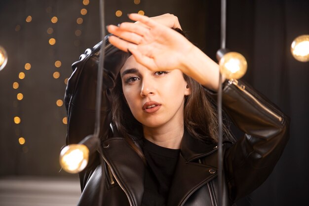 Portrait d'une belle jeune mannequin en blouson de cuir noir posant près des lampes.