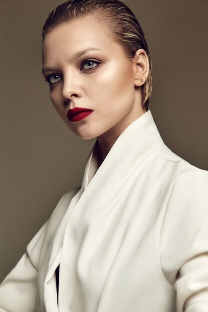 Portrait de la belle mode élégante femme brune modèle avec maquillage de soirée et lèvres rouges en veste blanche