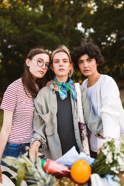 Photo gratuite portrait de belles filles avec vélo et panier plein de fleurs sauvages et de fruits regardant rêveusement à huis clos passer du temps ensemble dans le parc