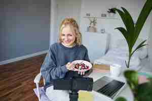 Photo gratuite portrait d'une blogueuse vloggeuse souriante tenant un bol avec un dessert et le montrant à la caméra au public.