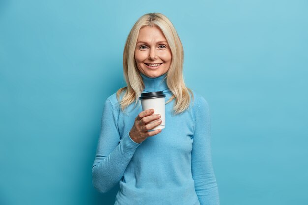 Portrait de bonne femme européenne adulte à la recherche d'une tasse de café jetable