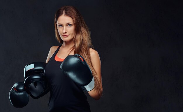 Le portrait d'une boxeuse portant des gants tient un casque de protection posant dans un studio. Isolé sur un fond texturé sombre.