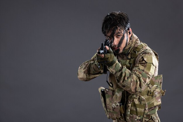 Portrait de brave soldat en camouflage avec mitrailleuse sur mur sombre