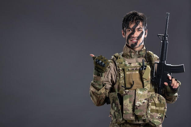 Photo gratuite portrait d'un brave soldat combattant avec une mitrailleuse en camouflage sur un mur sombre