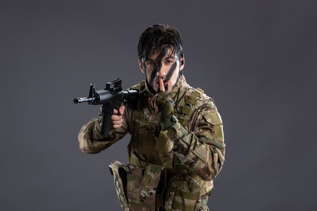 Portrait d'un brave soldat en tenue de camouflage lors d'une opération sur un mur sombre