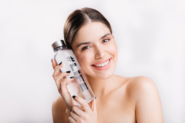 Photo gratuite portrait de brune sans maquillage de bonne humeur sur un mur isolé. femme positive avec une peau saine posant avec une bouteille d'eau avec la vie de hashtag.