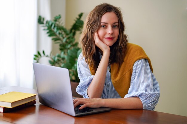 Portrait de bureau à domicile intérieur d'une influenceuse de blogs à la mode travaillant sur son ordinateur portable, vêtements élégants, intérieur minimaliste.