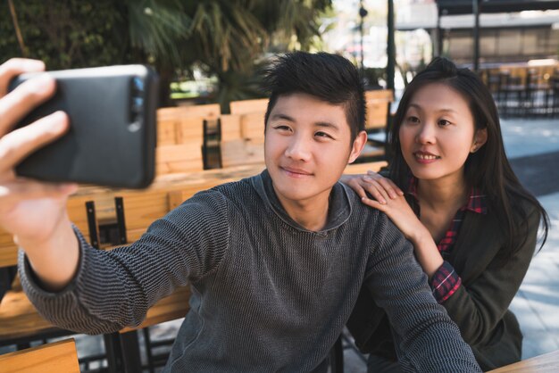 Portrait d'un charmant couple asiatique s'amuser et prendre un selfie avec un téléphone portable dans un café.