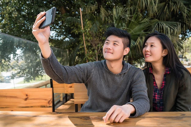Portrait d'un charmant couple asiatique s'amuser et prendre un selfie avec un téléphone portable dans un café.