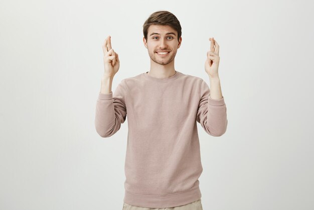 Portrait d'un charmant homme de race blanche avec des poils levant les mains avec les doigts croisés et souriant