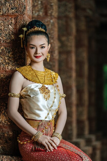 Portrait Charmante femme thaïlandaise en beau costume traditionnel, femme vêtue d'une robe thaïlandaise typique assise dans un site archéologique ou un temple thaïlandais, culture identitaire de la thaïlande