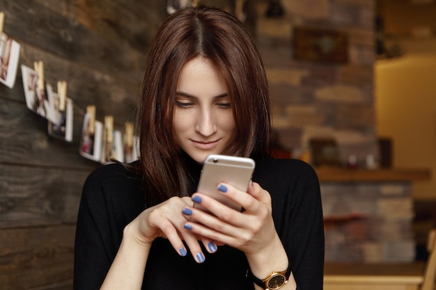 Portrait de charmante jeune femme européenne brune parcourant le fil d'actualité via les réseaux sociaux