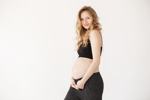 Portrait de charmante jeune maman aux cheveux blonds dans des vêtements noirs se tenant la main sous le ventre de femme enceinte